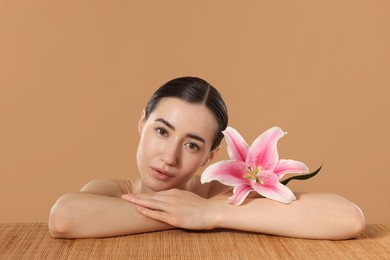 Photo of Beautiful woman after spa treatment with lily flower at bamboo table on beige background