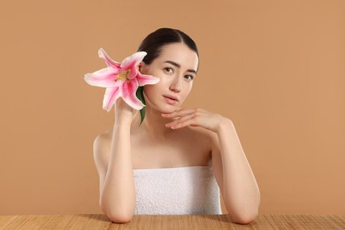 Photo of Beautiful woman after spa treatment with lily flower at bamboo table on beige background