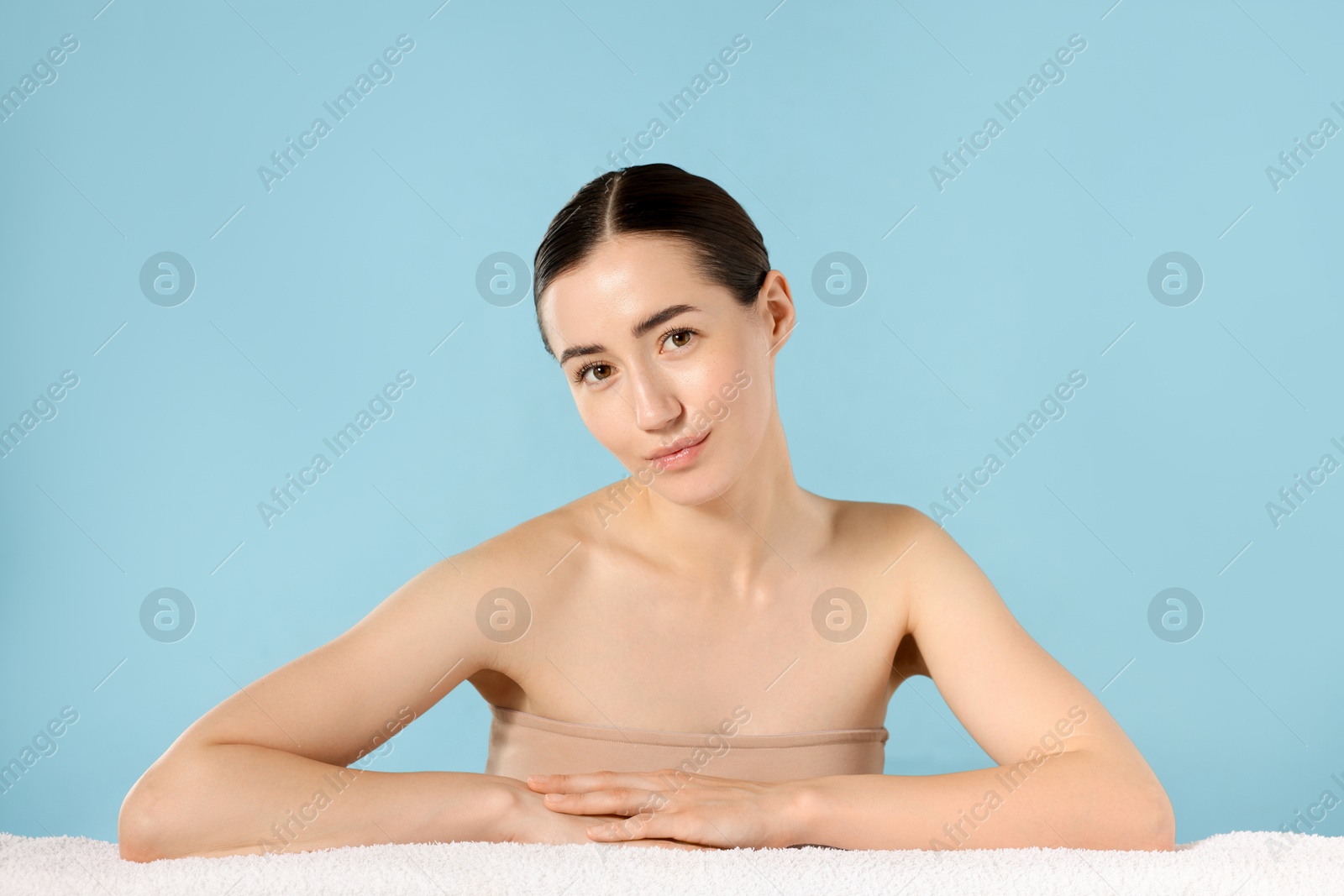 Portrait of beautiful woman with towel after spa treatment on light blue background Photo of Portrait of beautiful woman with towel after spa treatment on light blue background