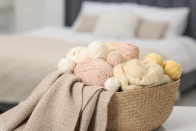 Photo of Felting wool and knitting yarn in wicker basket indoors, closeup