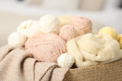 Photo of Felting wool and knitting yarn in wicker basket indoors, closeup