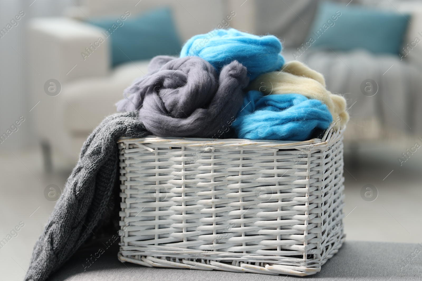 Photo of Soft felting wool in wicker basket on ottoman indoors, closeup