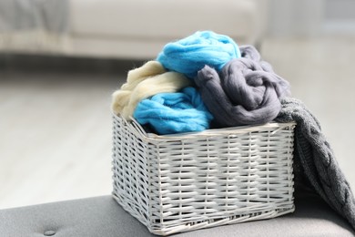Photo of Soft felting wool in wicker basket on ottoman indoors, closeup. Space for text