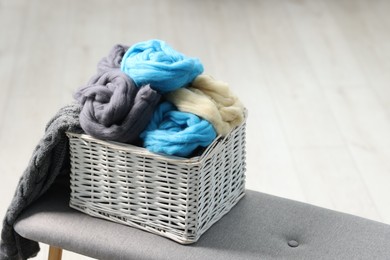 Photo of Soft felting wool in wicker basket on ottoman indoors, closeup. Space for text
