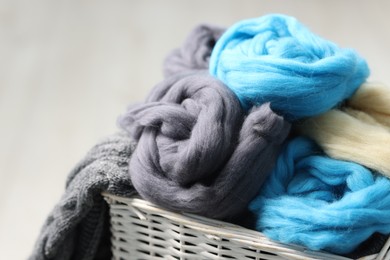 Photo of Soft felting wool in wicker basket on light grey background, closeup