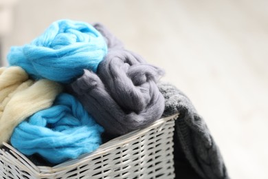 Photo of Soft felting wool in wicker basket on light grey background, closeup. Space for text