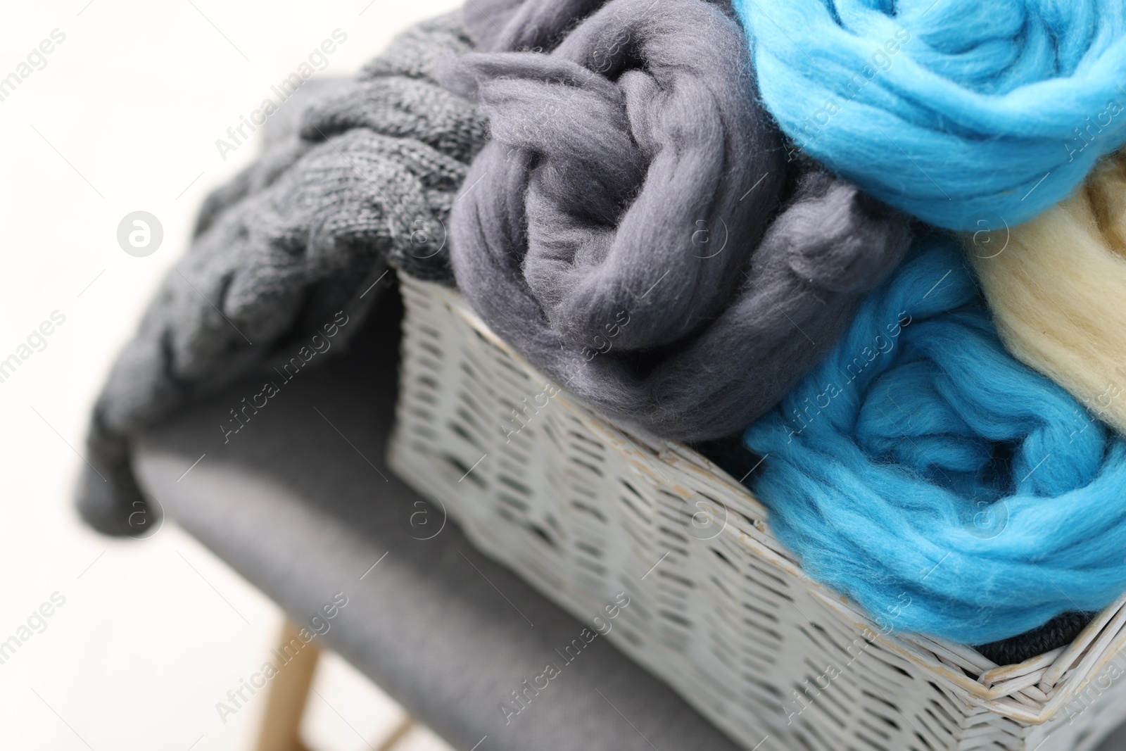 Photo of Soft felting wool in wicker basket on light grey background, closeup