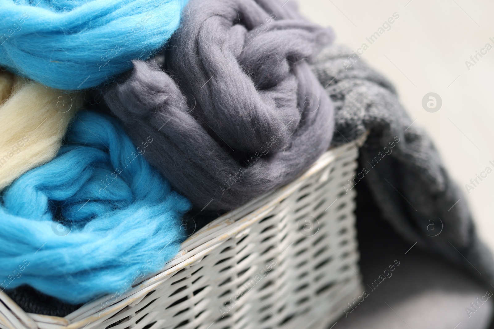 Photo of Soft felting wool in wicker basket on light grey background, closeup