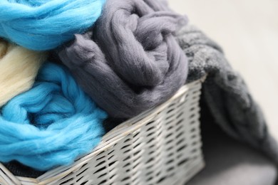 Photo of Soft felting wool in wicker basket on light grey background, closeup