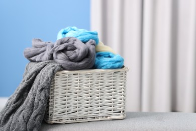 Photo of Soft felting wool in wicker basket on ottoman indoors, closeup. Space for text