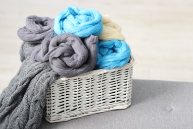 Photo of Soft felting wool in wicker basket on ottoman indoors, closeup. Space for text