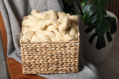 Photo of Soft felting wool in wicker basket on chair indoors, closeup