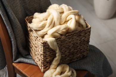 Photo of Soft felting wool in wicker basket on chair indoors, closeup