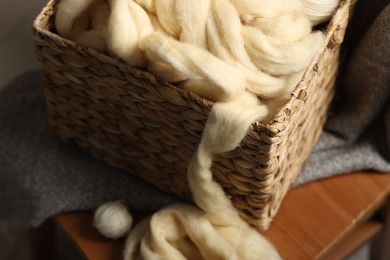 Photo of Soft felting wool in wicker basket on chair indoors, closeup