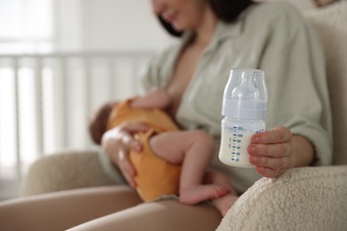Photo of Mother with bottle of milk breastfeeding her newborn baby at home, selective focus