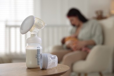 Photo of Breast pump with milk on table. Mother breastfeeding her baby at home, selective focus