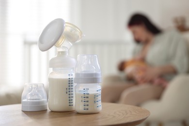Photo of Breast pump and bottle with milk on table. Mother breastfeeding her baby at home, selective focus