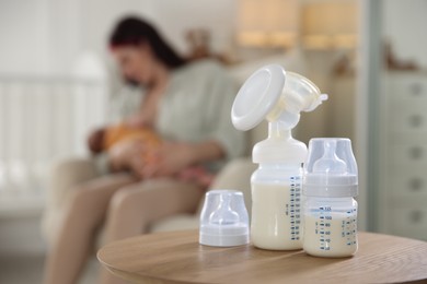 Photo of Breast pump and bottle with milk on table. Mother breastfeeding her baby at home, selective focus