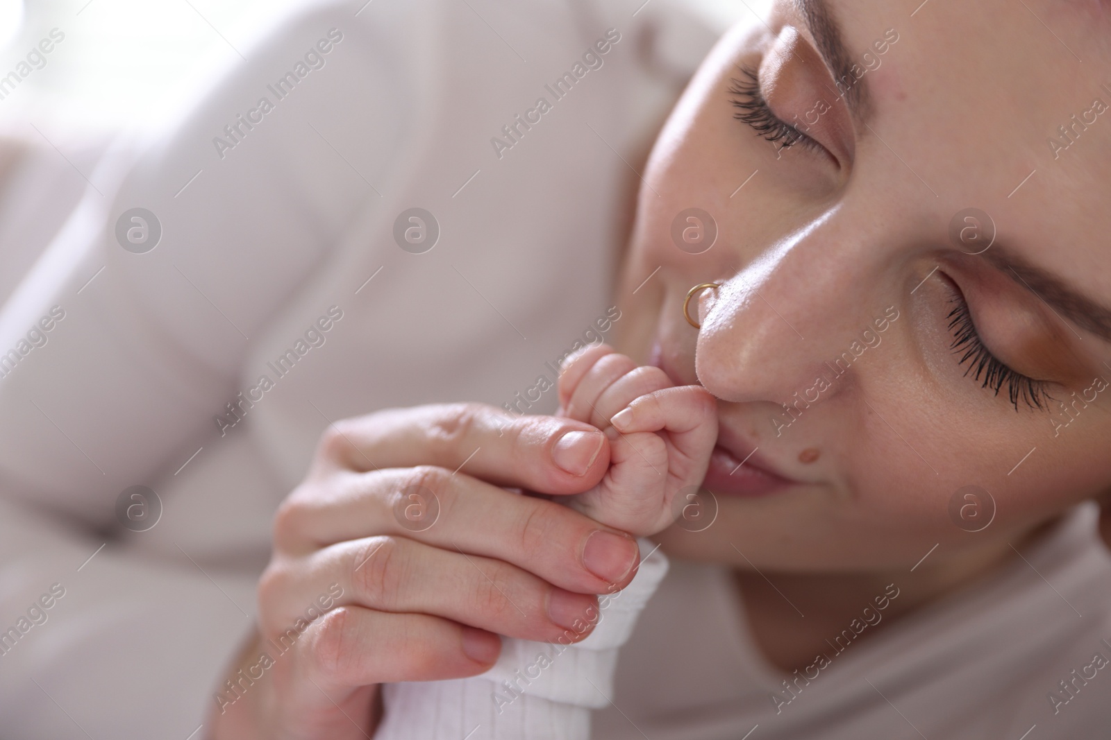 Mother kissing her baby's hand indoors, closeup Photo of Mother kissing her baby's hand indoors, closeup