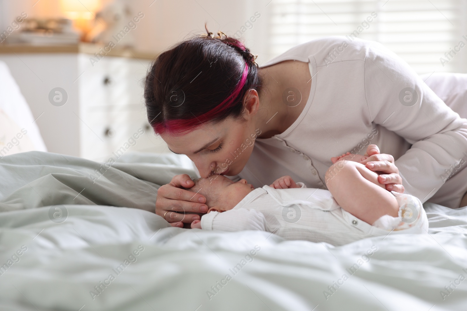 Mother putting her cute newborn baby to sleep on bed at home Photo of Mother putting her cute newborn baby to sleep on bed at home