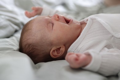 Photo of Cute newborn baby yawning on bed, closeup
