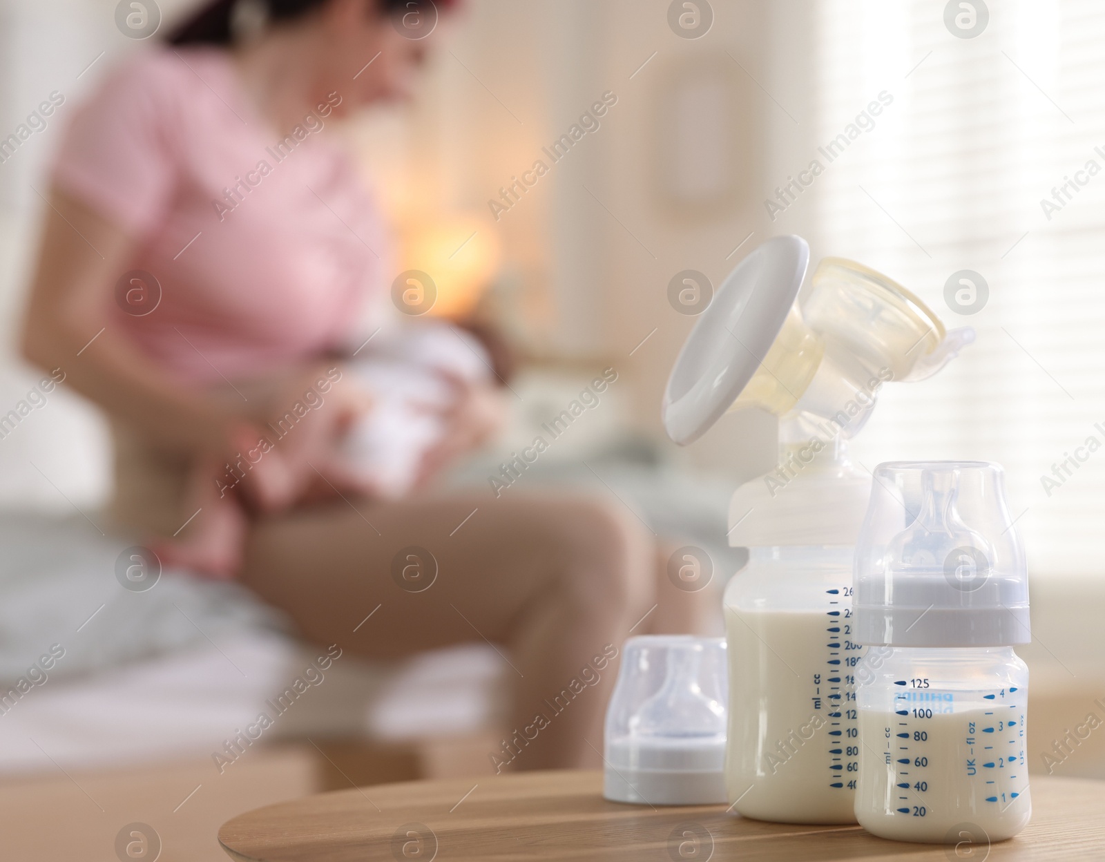 Breast pump and bottle with milk on table. Mother breastfeeding her baby at home, selective focus Photo of Breast pump and bottle with milk on table. Mother breastfeeding her baby at home, selective focus