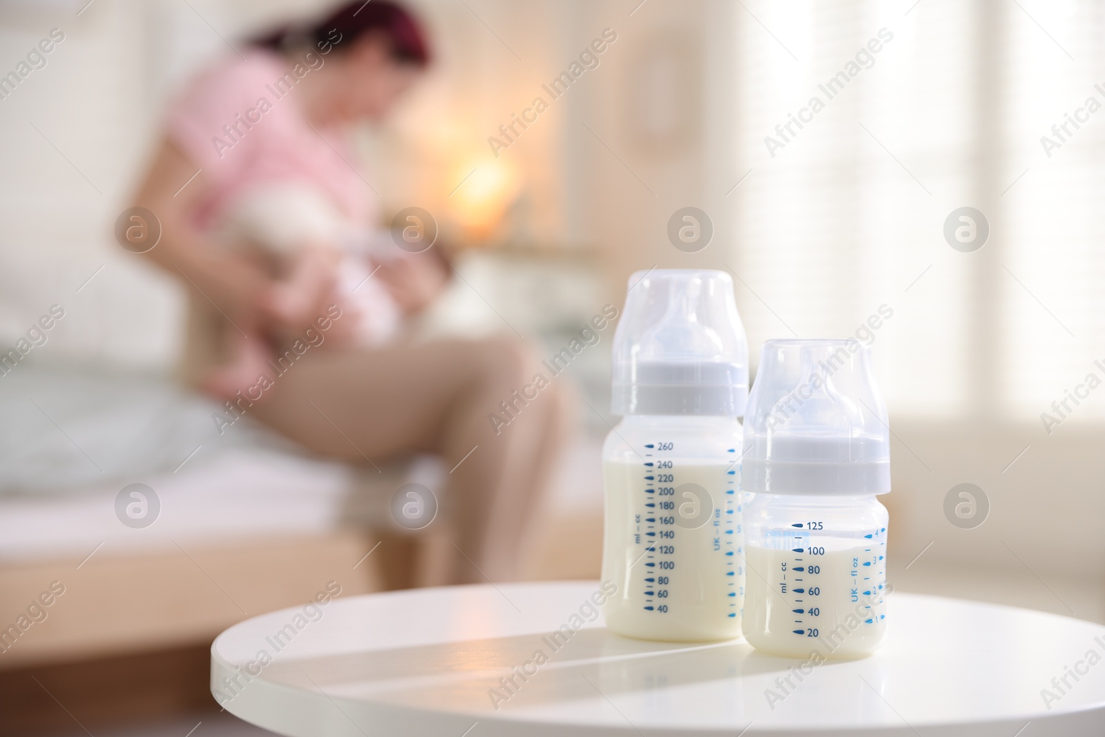 Bottles with milk on table. Mother breastfeeding her baby at home, selective focus Photo of Bottles with milk on table. Mother breastfeeding her baby at home, selective focus