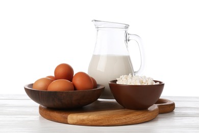 Photo of Milk, cottage cheese and eggs on wooden table against white background