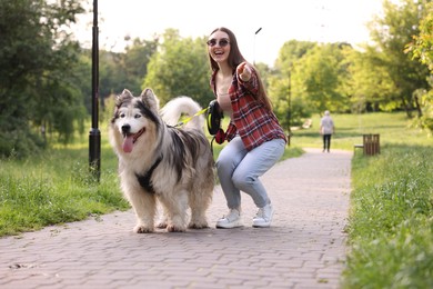 Photo of Happy woman showing something to her cute Alaskan malamute dog in park