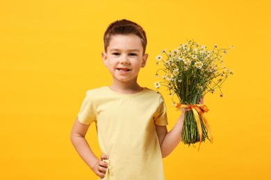 Photo of Smiling little boy with bouquet of beautiful chamomile flowers on yellow background