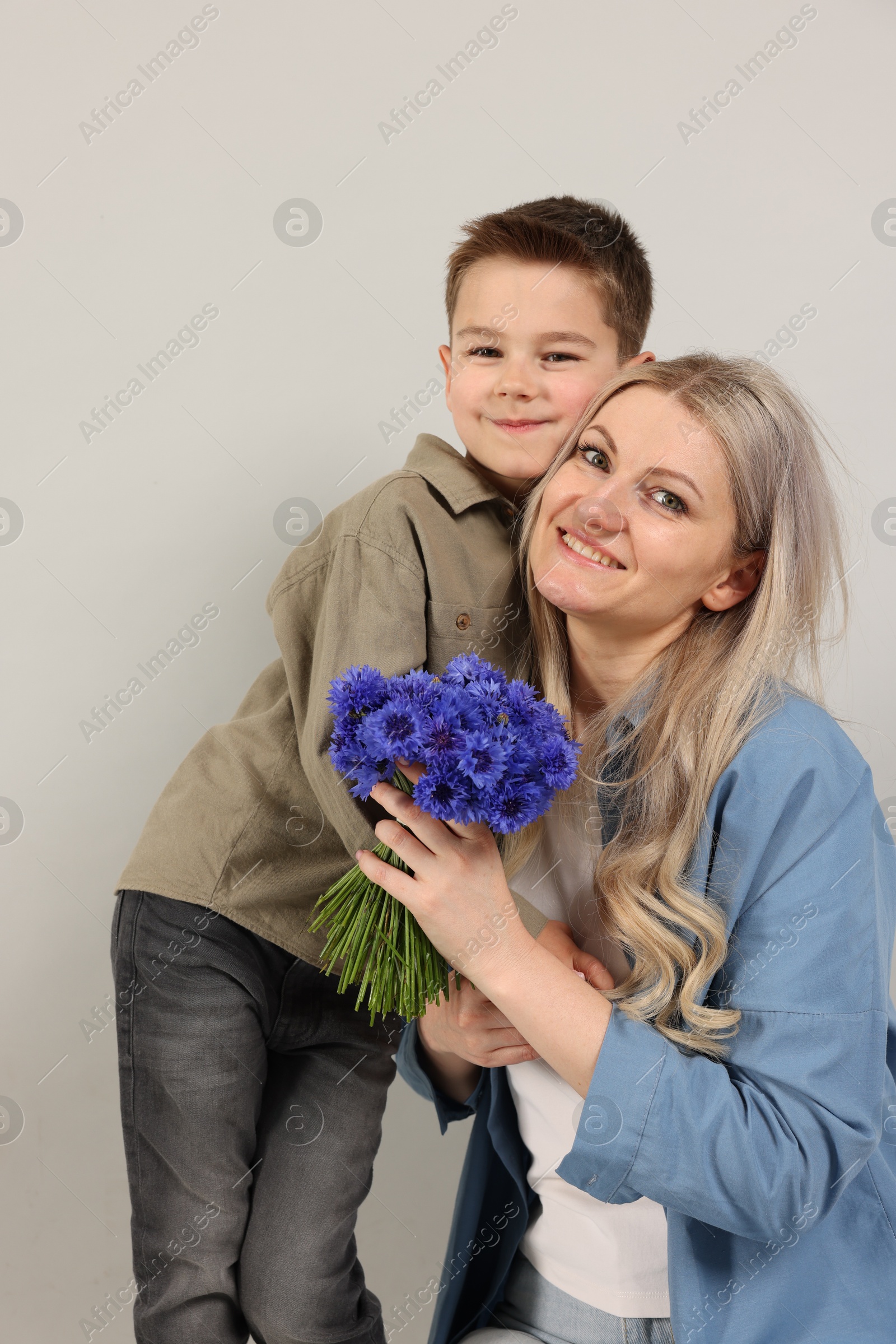 Little boy and his smiling mother with bouquet of beautiful cornflowers on grey background Photo of Little boy and his smiling mother with bouquet of beautiful cornflowers on grey background