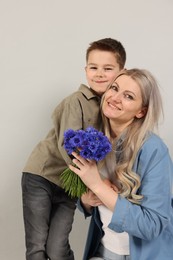Photo of Little boy and his smiling mother with bouquet of beautiful cornflowers on grey background