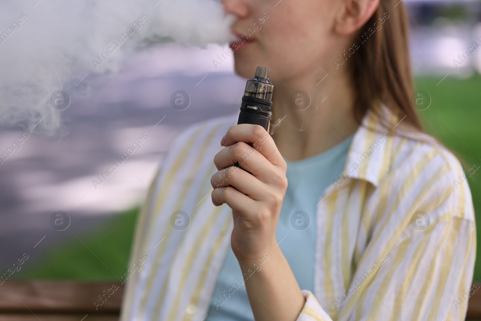 Young woman using electronic smoking device outdoors, closeup. Space for text Photo of Young woman using electronic smoking device outdoors, closeup. Space for text