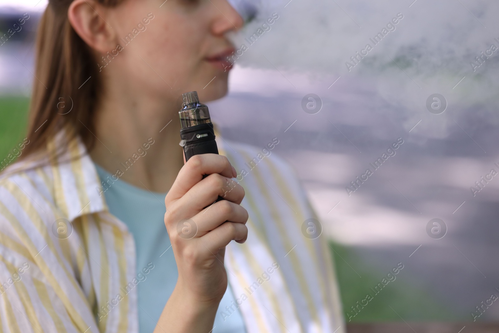 Young woman using electronic smoking device outdoors, closeup. Space for text Photo of Young woman using electronic smoking device outdoors, closeup. Space for text
