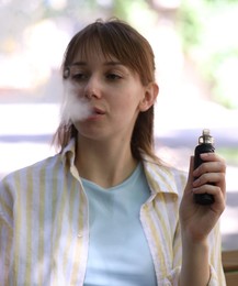 Photo of Young woman using electronic smoking device outdoors