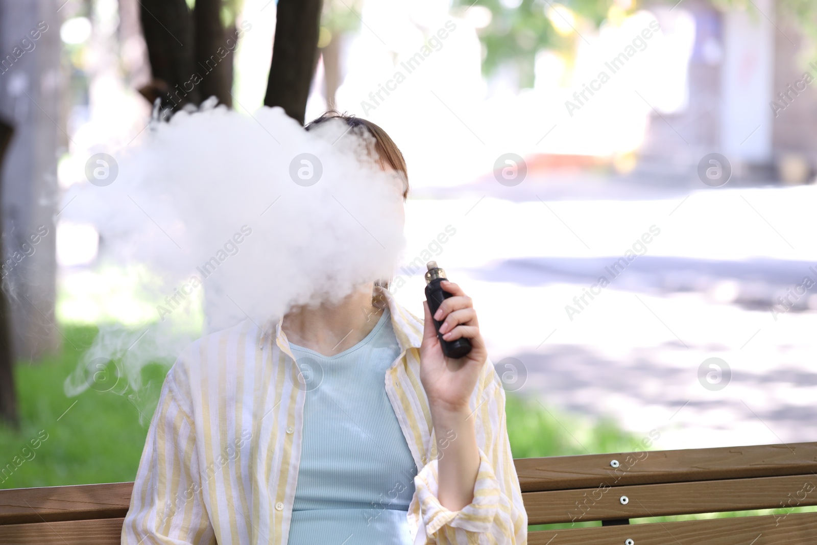 Young woman using electronic smoking device outdoors. Space for text Photo of Young woman using electronic smoking device outdoors. Space for text