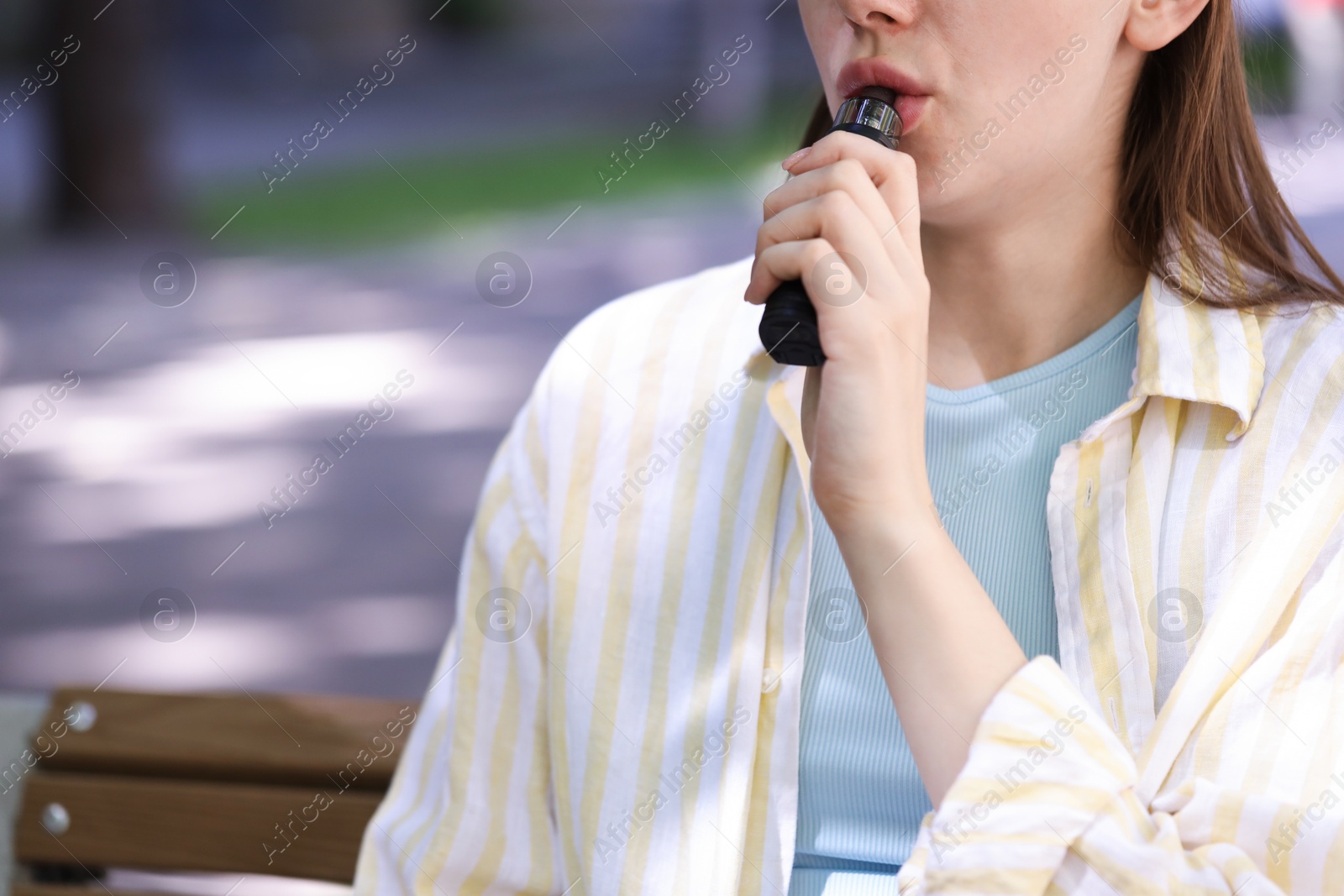 Young woman using electronic smoking device outdoors, closeup. Space for text Photo of Young woman using electronic smoking device outdoors, closeup. Space for text
