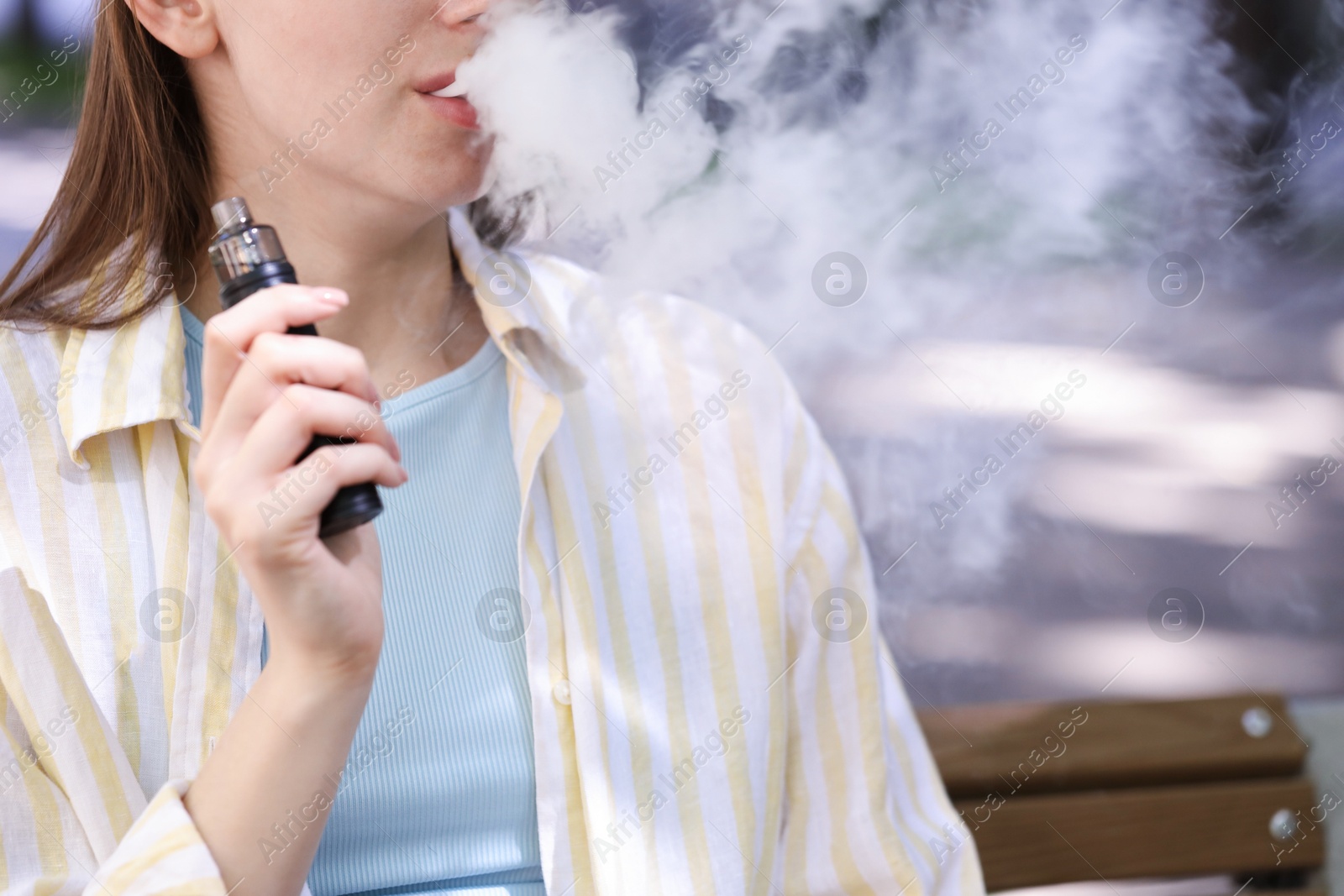 Young woman using electronic smoking device outdoors, closeup. Space for text Photo of Young woman using electronic smoking device outdoors, closeup. Space for text