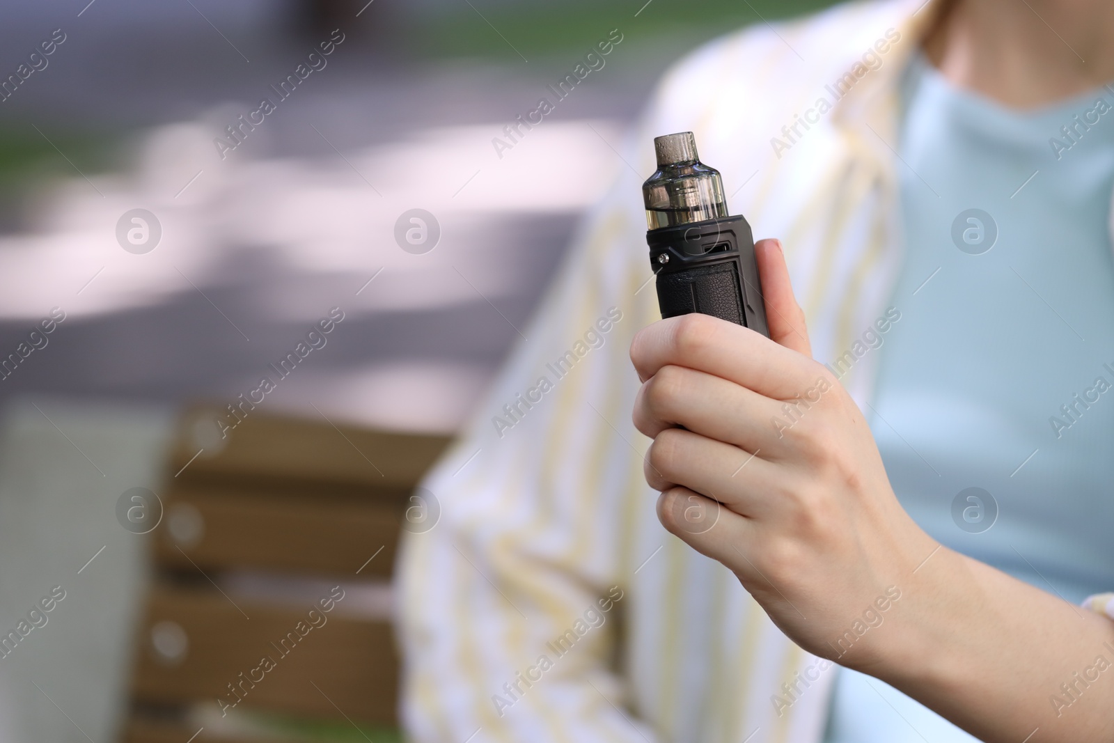 Young woman with electronic smoking device outdoors, closeup. Space for text Photo of Young woman with electronic smoking device outdoors, closeup. Space for text