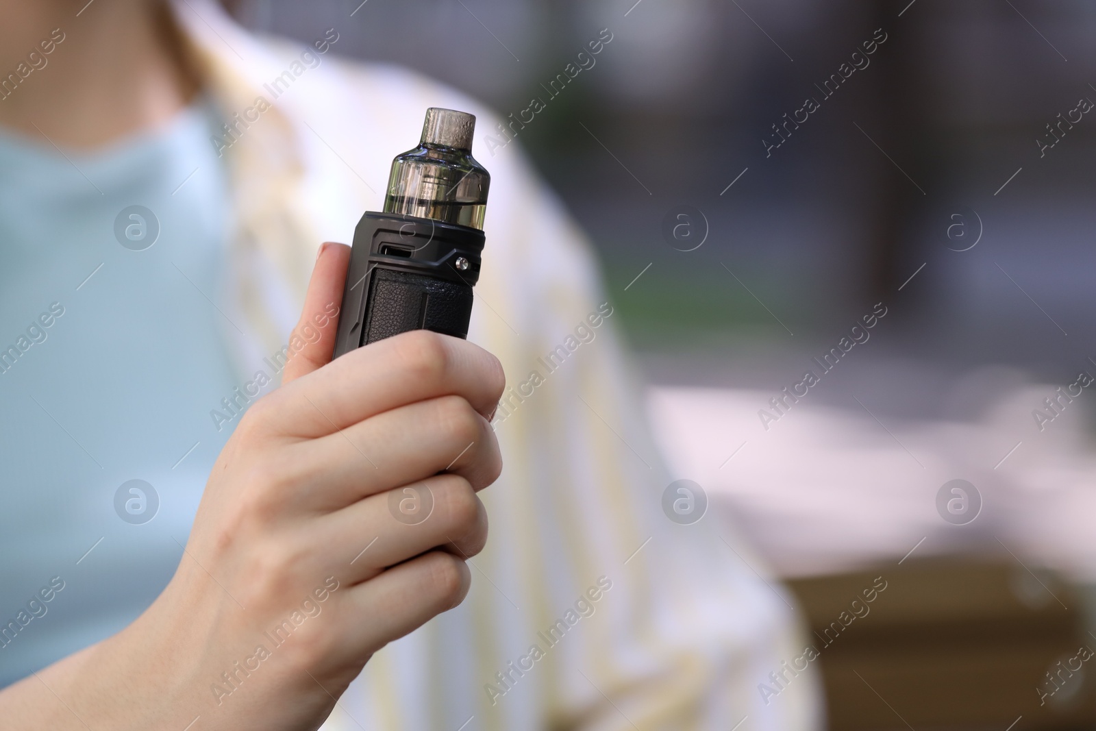 Young woman with electronic smoking device outdoors, closeup. Space for text Photo of Young woman with electronic smoking device outdoors, closeup. Space for text