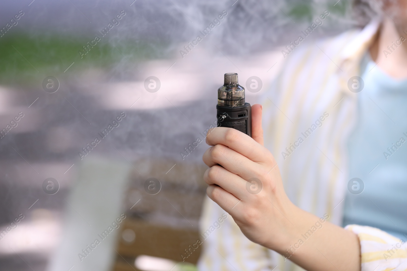 Young woman with electronic smoking device outdoors, closeup. Space for text Photo of Young woman with electronic smoking device outdoors, closeup. Space for text