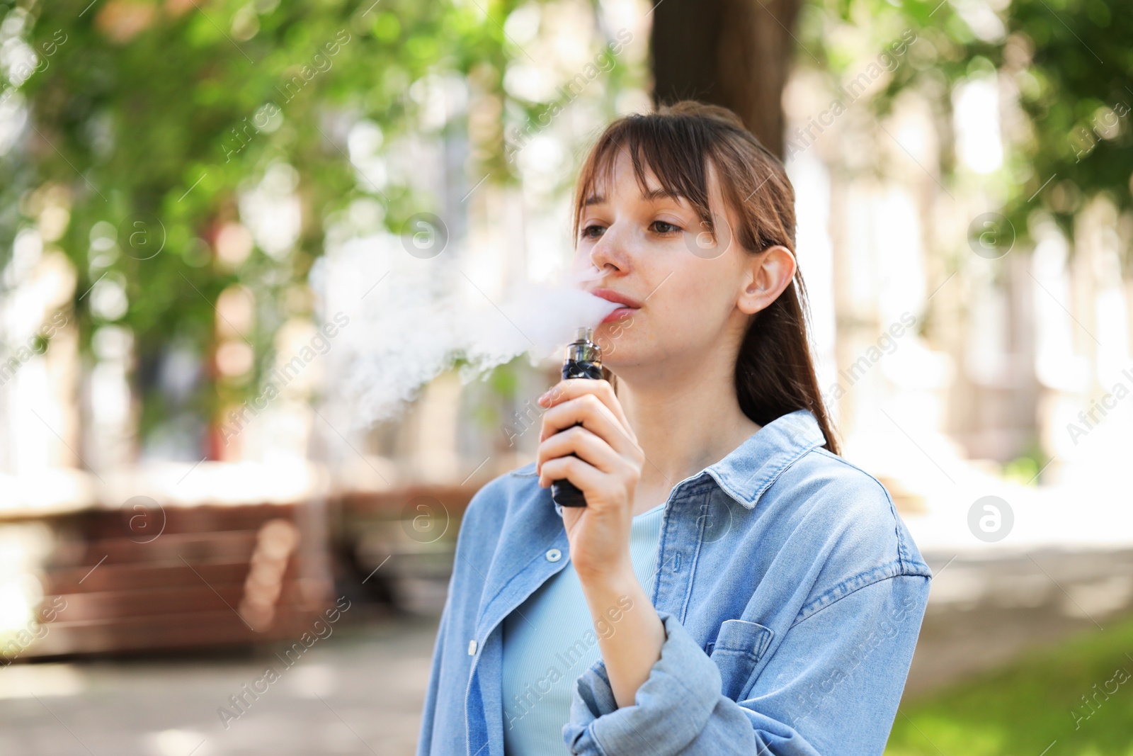Young woman using electronic smoking device outdoors. Space for text Photo of Young woman using electronic smoking device outdoors. Space for text