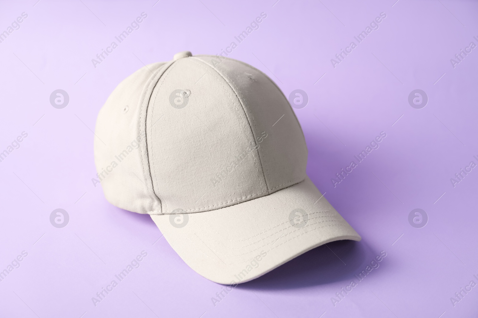 One beige baseball hat on violet background Photo of One beige baseball hat on violet background
