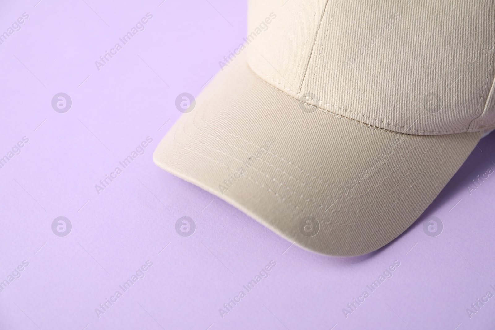 Beige baseball hat on violet background, closeup. Space for text Photo of Beige baseball hat on violet background, closeup. Space for text