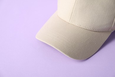 Photo of Beige baseball hat on violet background, closeup. Space for text