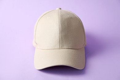 Photo of Beige baseball hat on violet background, closeup