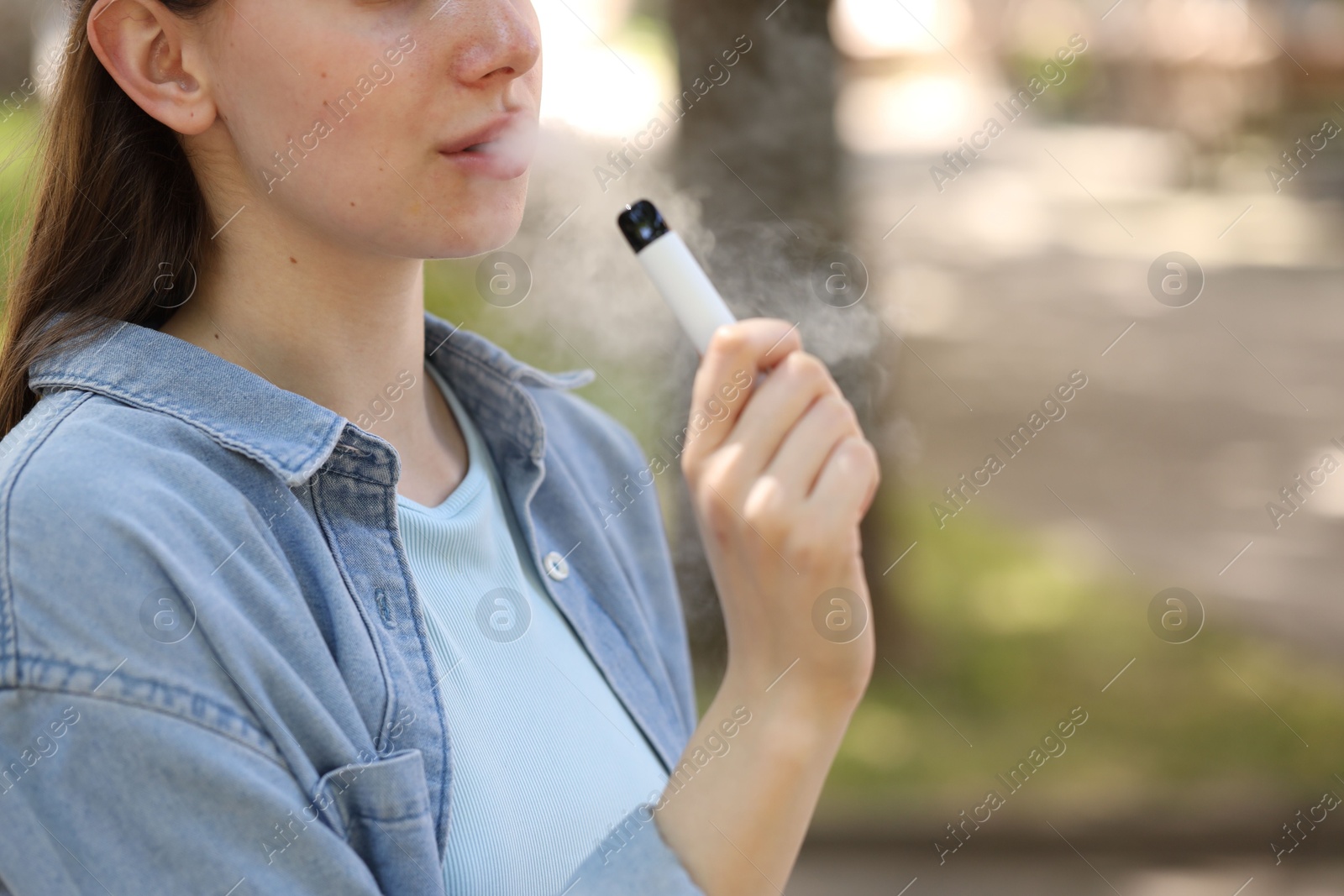 Young woman using electronic smoking device outdoors, closeup. Space for text Photo of Young woman using electronic smoking device outdoors, closeup. Space for text