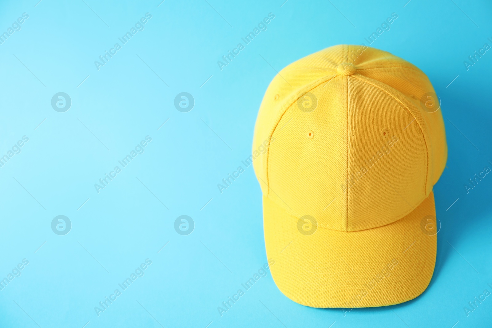 Photo of Yellow baseball hat on light blue background, above view. Space for text