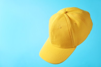 Photo of Yellow baseball hat in air on light blue background, space for text