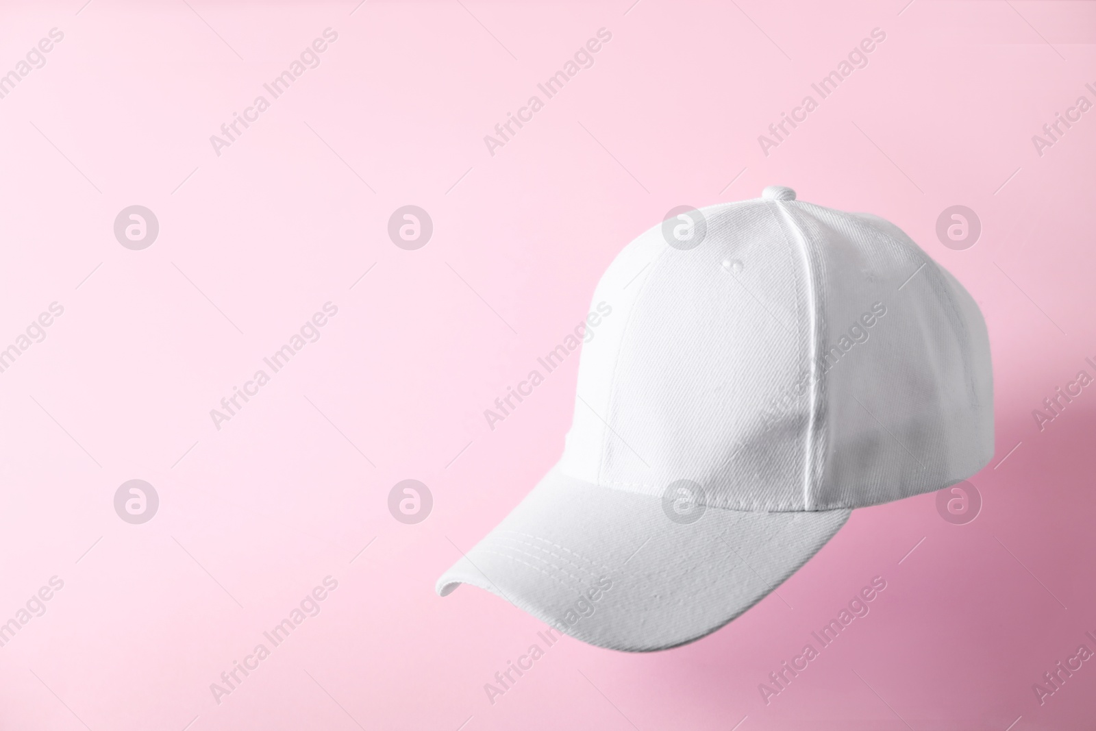 Photo of White baseball hat in air on pink background, space for text